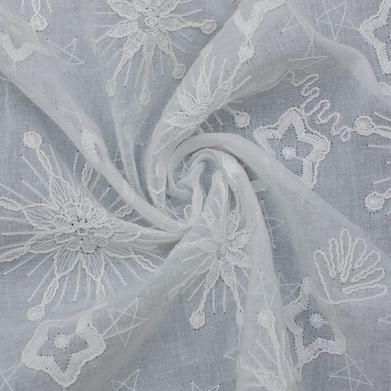 Delicate white embroidered lace fabric adorned with a floral pattern, made of cotton.