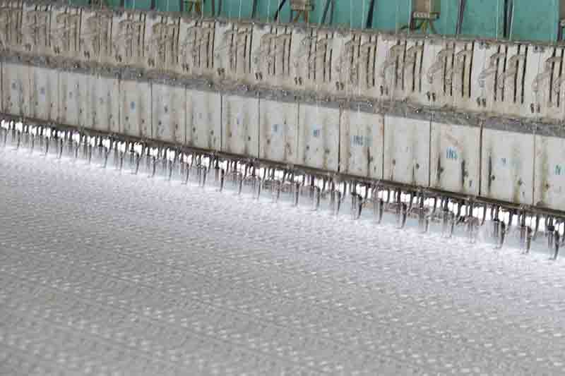 A large machine with numerous threads, used for creating custom lace fabric