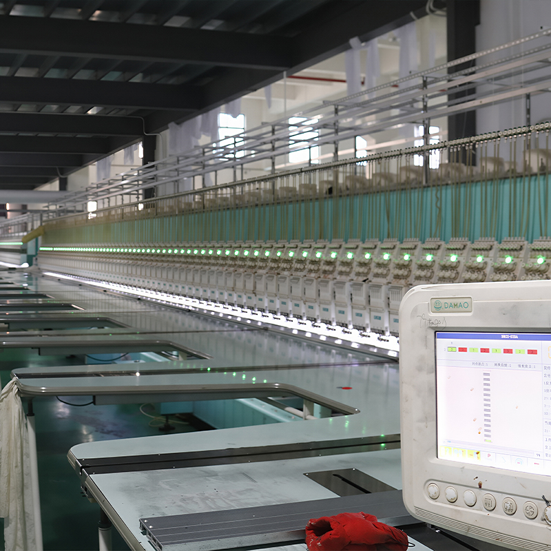 A machine operates in the Yituo embroidery factory, surrounded by various other machines in a busy industrial setting