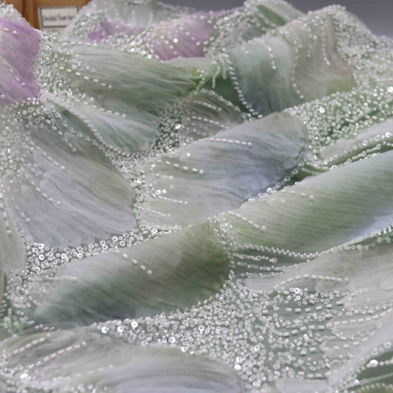 A vibrant purple flower with pearl accents, artistically displayed on a textured polyester lace fabric background