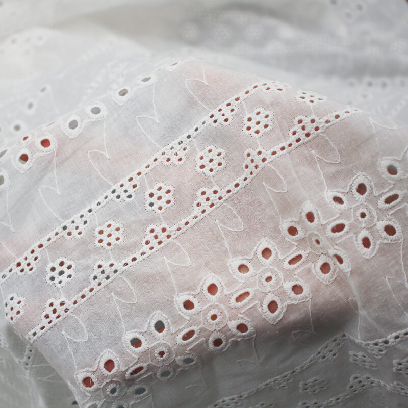 Cotton lace fabric in white, embellished with a design of black dots