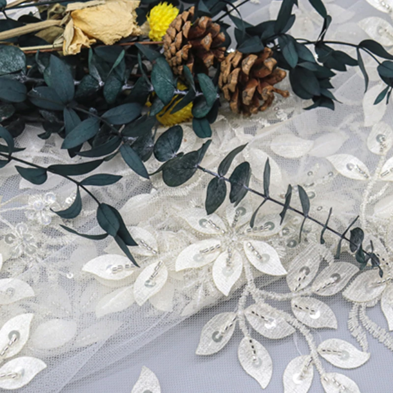 Detailed view of white lace fabric adorned with sequins and delicate white flowers