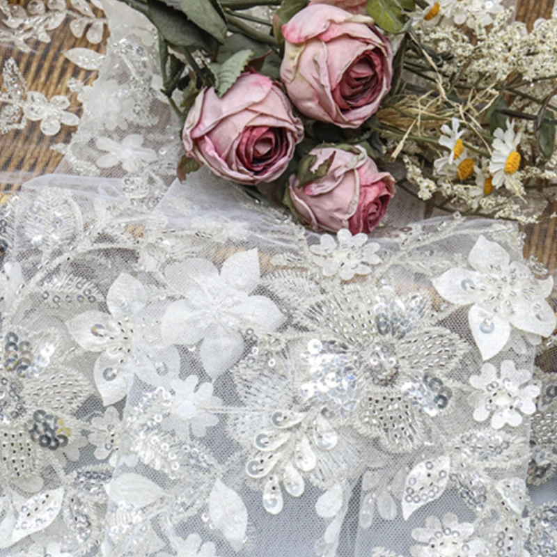 Detailed view of white lace fabric adorned with sequins and floral designs
