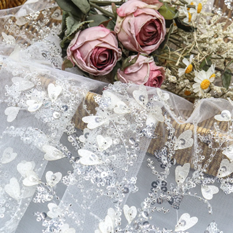 Silver sequin lace fabric adorned with white flowers and leaves, creating a shimmering and elegant design