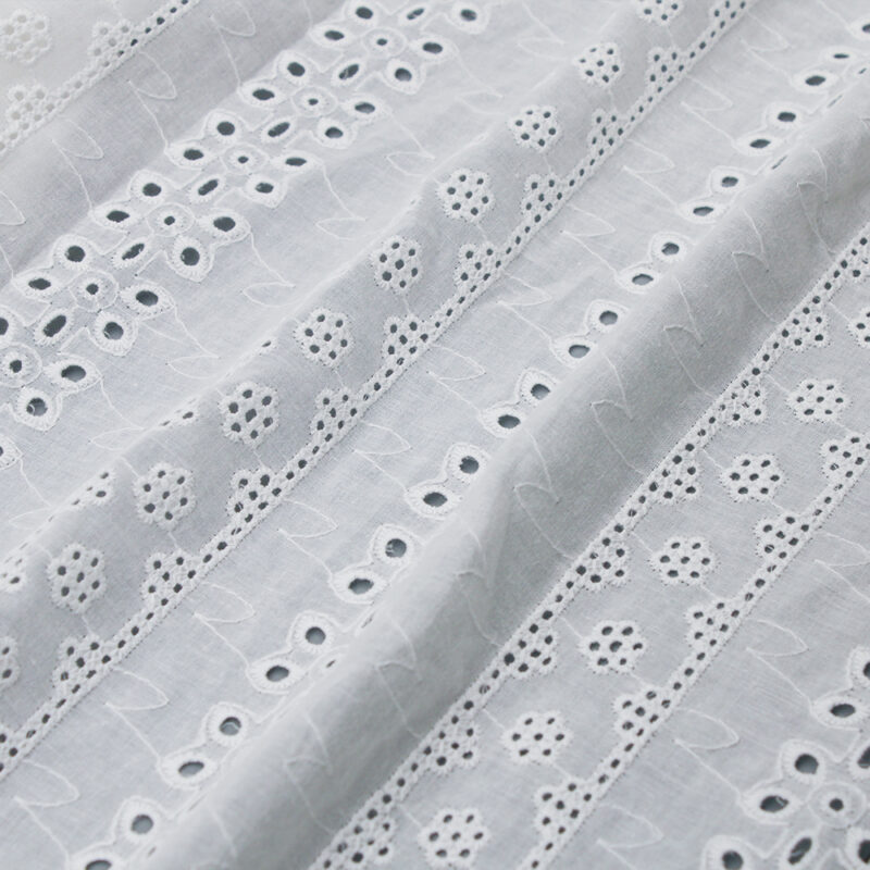 White cotton lace fabric featuring small holes and dots, creating a delicate and intricate pattern